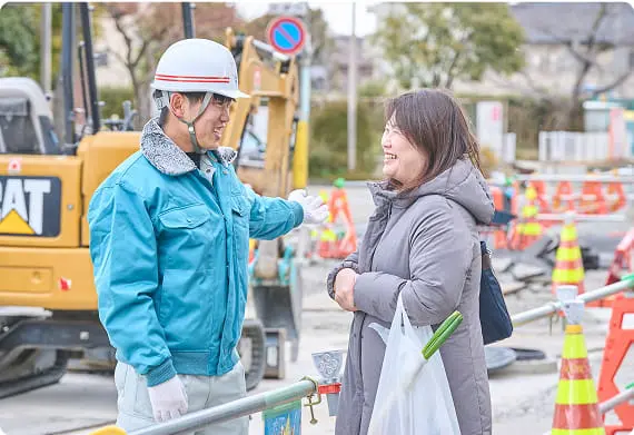 工事現場で通行人の女性と会話をする作業員男性
